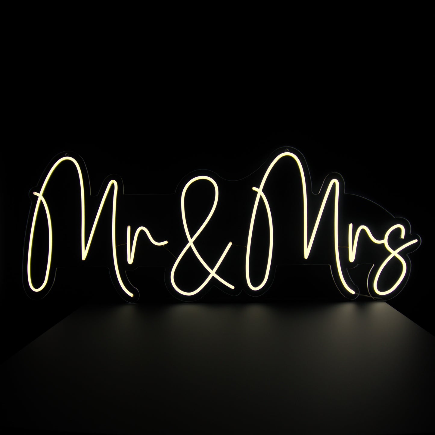A neon sign with the words 'Mr & Mrs' written in a cursive script, illuminated in bright white against a black background.