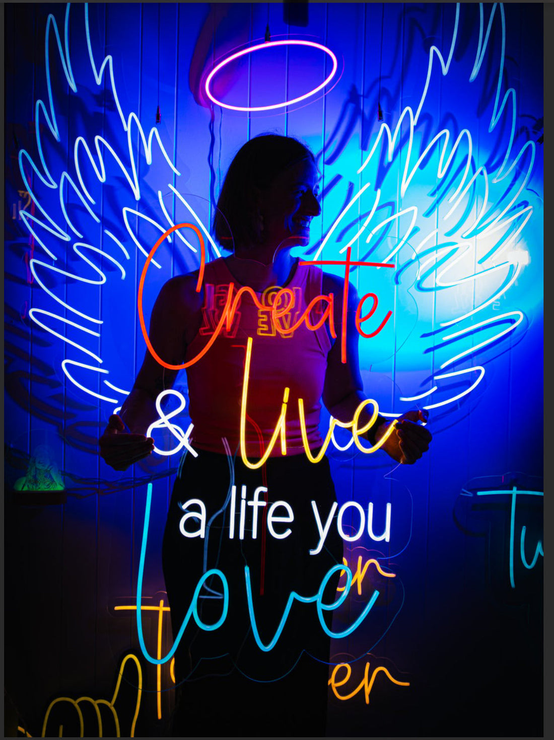 Neon angel wings and halo with the words Create and live a life you love, with a woman standing in front