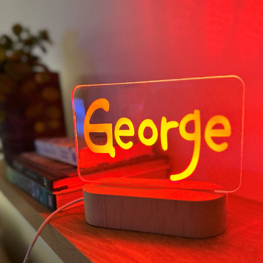 Personalised night light with the name George glowing orange on a timber base