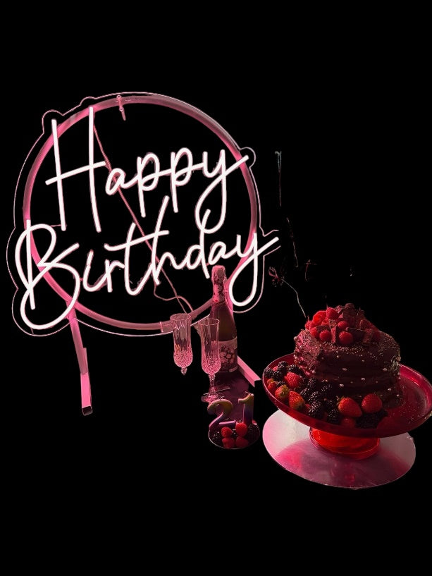 A beautiful happy birthddayneon on display next to a adorable cake