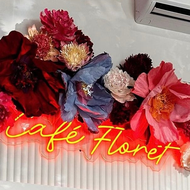 Red script neon sign reading Café Floret under a display of bright flowers