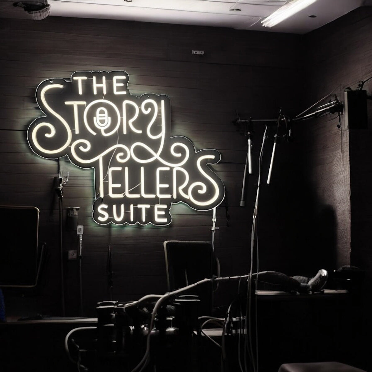 Warm white neon sign reading The Story Tellers Suite in a podcast studio