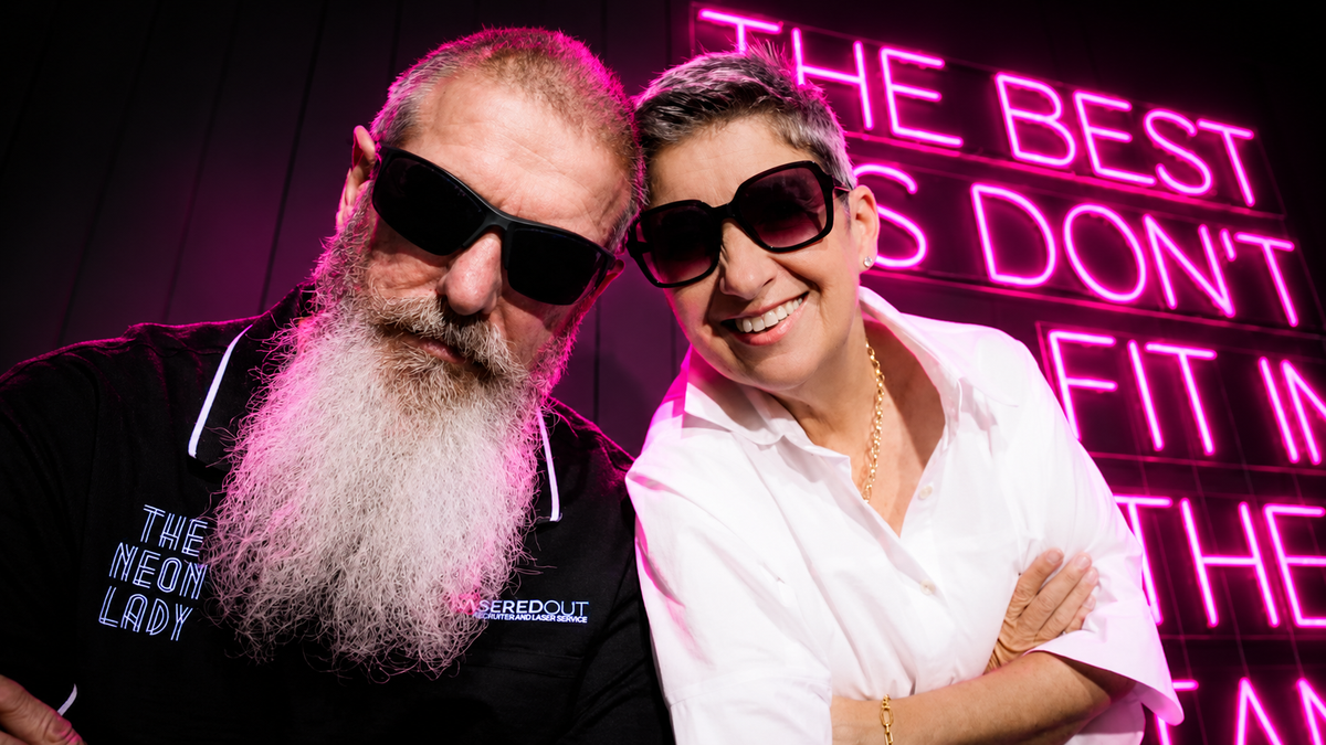 Shaz smiling with Russell under the hot pink neon sign in The Neon Lady showroom