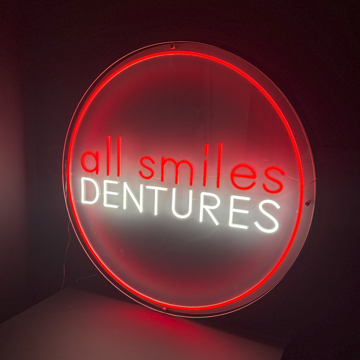 Round red and white neon sign reading all smiles dentures