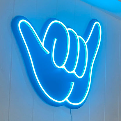 illuminated blue neon shaka hand light mounted on a wall