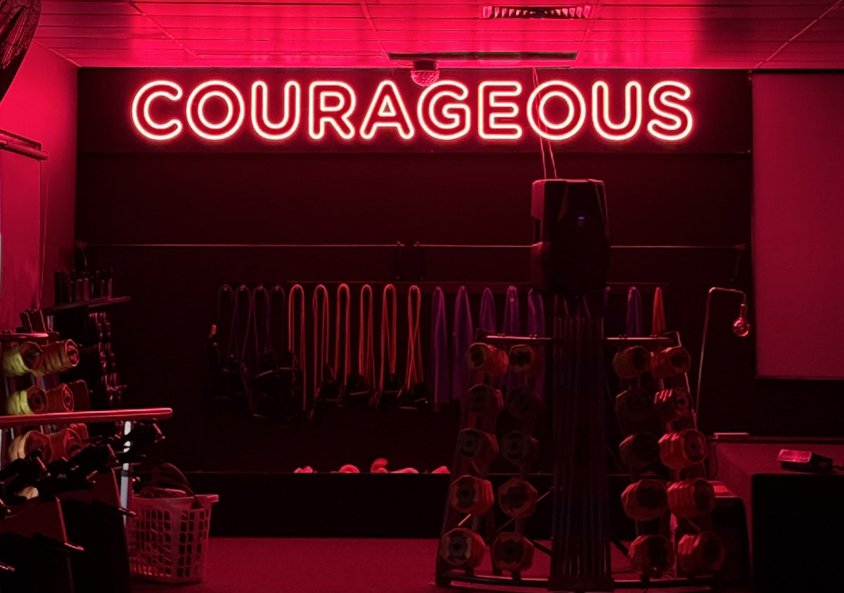 Red LED neon sign reading Courageous above the weights area of a gym