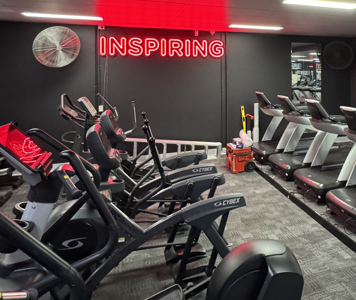 Red LED neon sign reading Inspiring above the cardio machines at a Fernwood gym