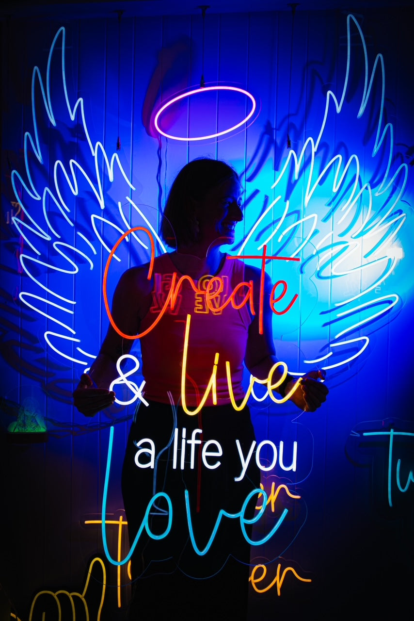 Neon angel wings and halo with the words Create and live a life you love, with a woman standing in front