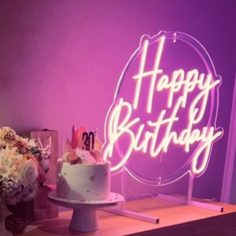 pink happy birthday neon sign giving a warm glow, sitting on the cake and present table.