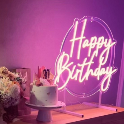 pink happy birthday neon sign giving a warm glow, sitting on the cake and present table.
