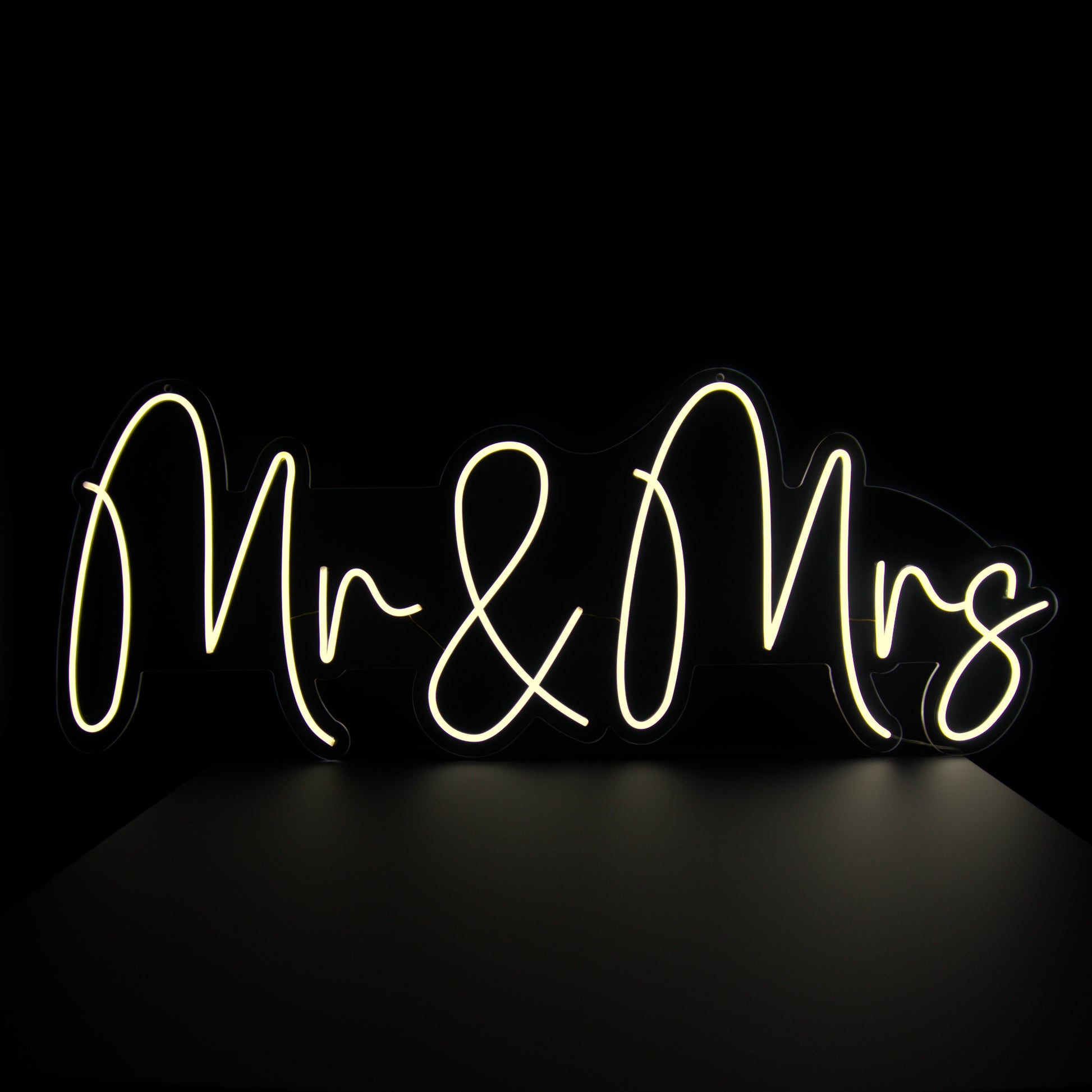 A neon sign with the words 'Mr & Mrs' written in a cursive script, illuminated in bright white against a black background.