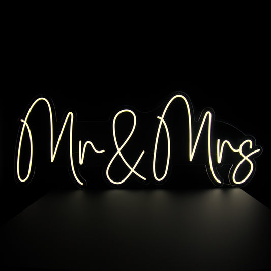 A neon sign with the words 'Mr & Mrs' written in a cursive script, illuminated in bright white against a black background.