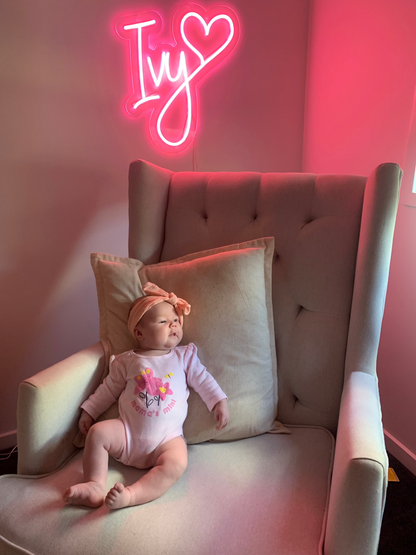 baby girl sitting on an armchair under a pink neon glowing neon sign