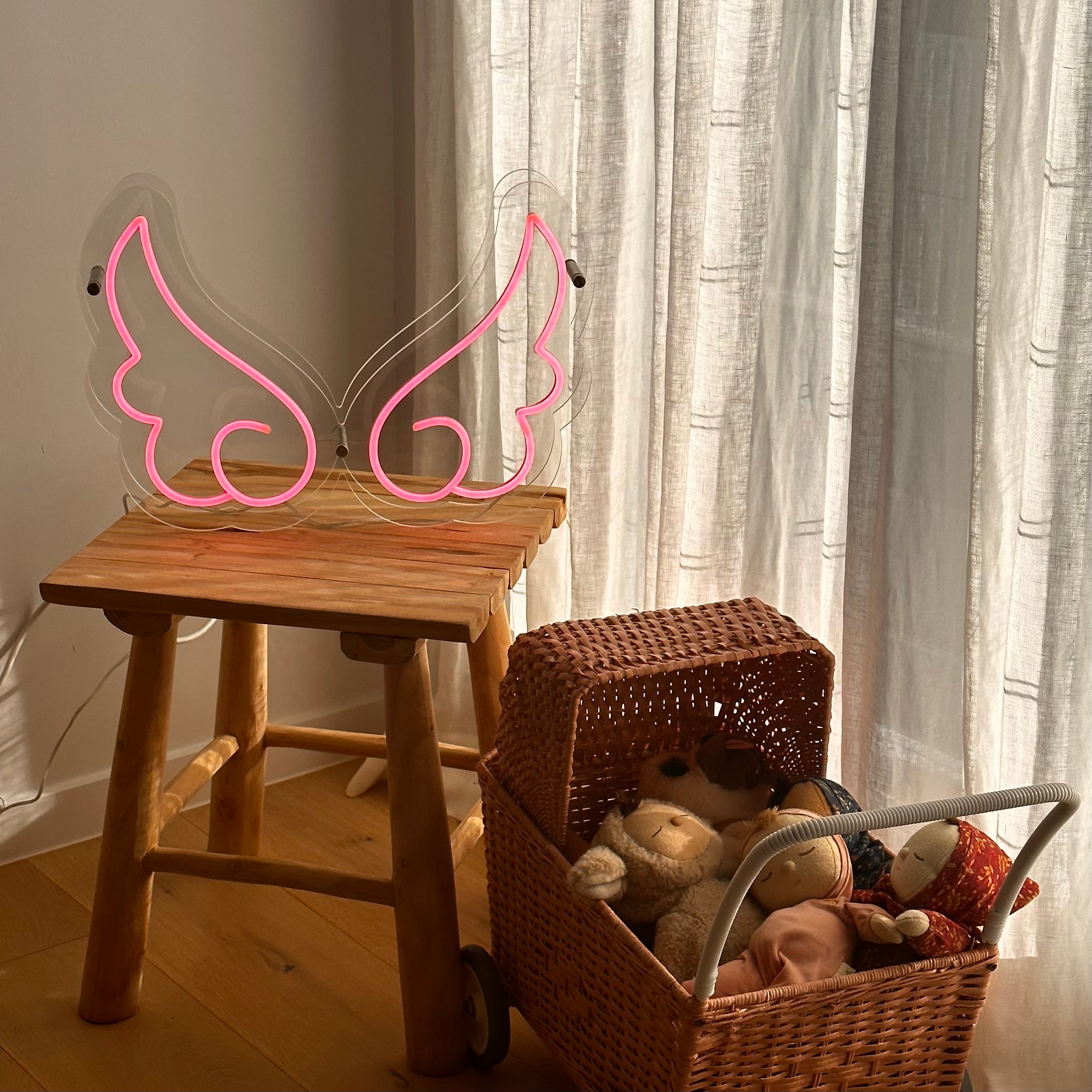 clear-acrylic-angel-wing-shape-neon-table-light-in-a-playroom-next-to-a-pram-filled-with-dolls