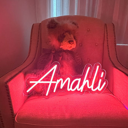 personalised Amahli pink neon light on a armchair leaning against a teddy bear.