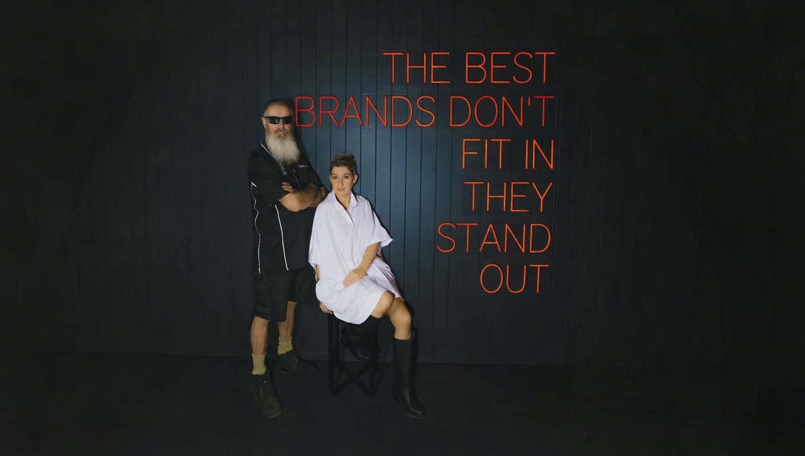 The best brands don't fit in, they stand out: red neon sign switching on behind two people in a dark studio