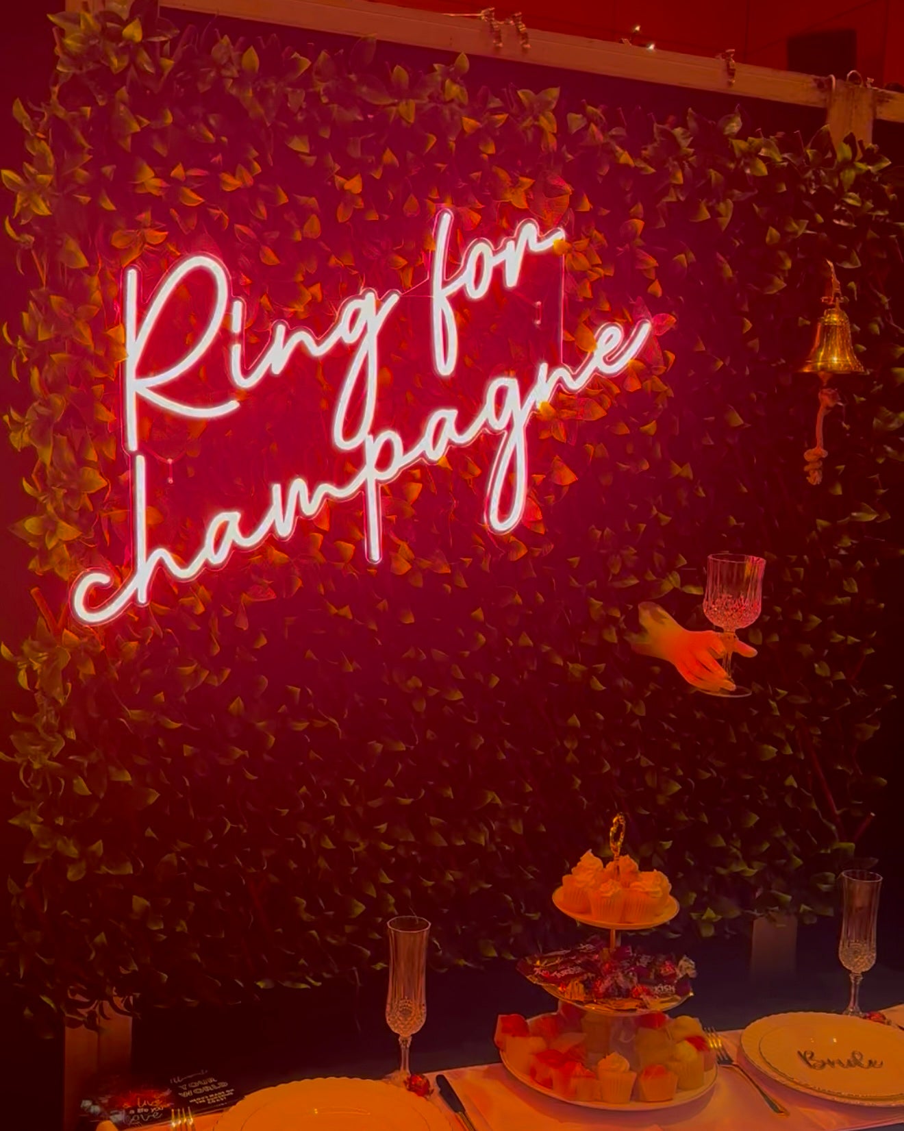Neon sign reading 'Ring for Champagne' on a decorative wall with a table setup.