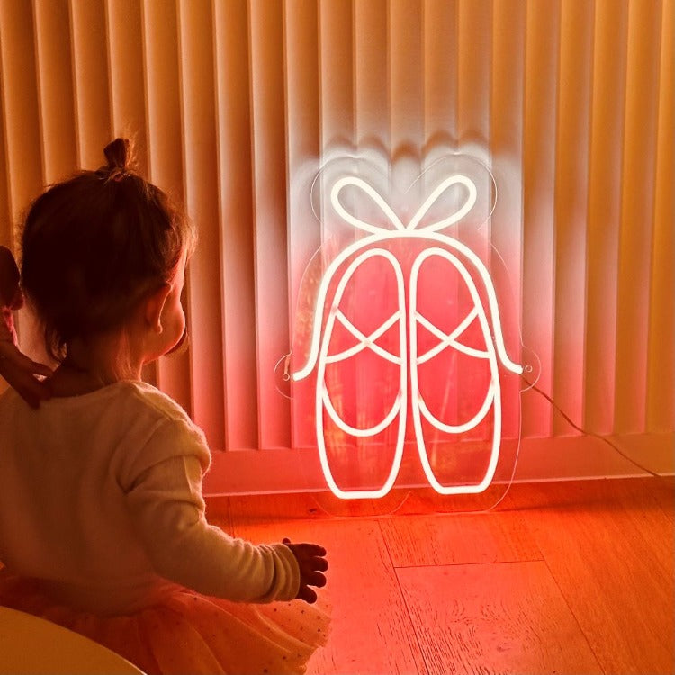 little-girl-looking-at-pair-of-pink-and-ballet-slippers-neon-sign-leaning-on-a-wall