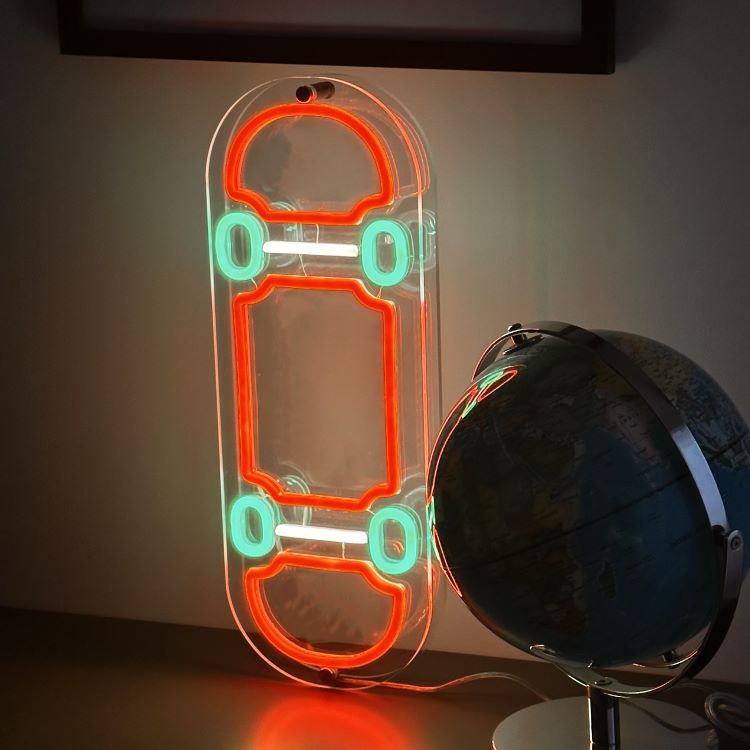 orange-and-green-neon-skateboard-sign-standing-vertical-on-a-desk-next-to-a-globe