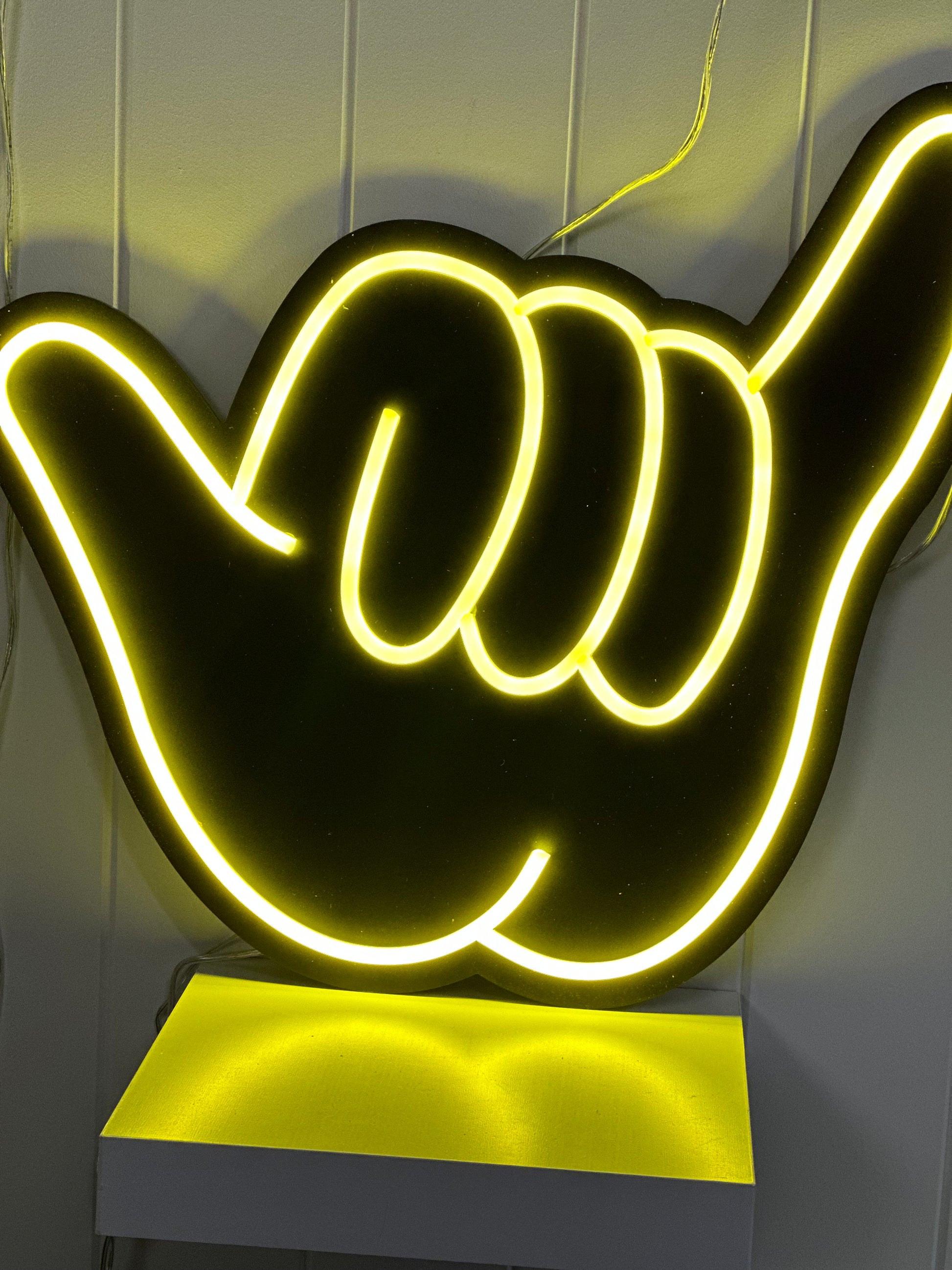 Yellow noen shaka hand on a matte black backing board